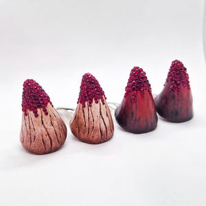 May include: Four conical horn-shaped accessories arranged in a row. Each piece features a textured, wood-like base in shades of brown and red, topped with a cluster of small, sparkling red crystals that resemble a dripping or encrusted effect.