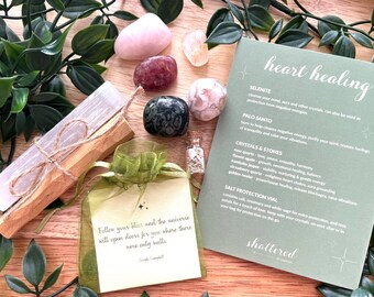 May include: A heart healing crystal kit with a selenite wand, palo santo stick, rose quartz, flower agate, kyanite, strawberry quartz, golden healer, and a salt protection vial. The kit comes with a card that says "heart healing" and lists the crystals and their properties. The card also includes a quote: "Follow your bliss and the universe will open doors for you where there were only walls."