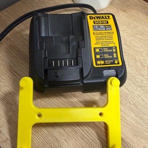 May include: A black and yellow DeWalt DCB107 12V/20V Max Lithium Ion battery charger with a yellow plastic support. The charger has indicator lights for charging status and safety information. The support is in the shape of an H.