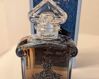 May include: A clear glass bottle of perfume with a silver cap and a black label that says "La Petite Robe Noire" by Guerlain. The bottle is sitting on a white surface.