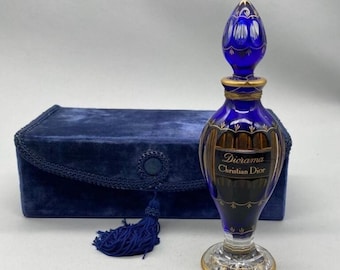 May include: A cobalt blue Diorama Christian Dior perfume bottle with gold accents and a matching blue velvet case. The bottle has a decorative stopper and a clear glass base. The case has a tassel.