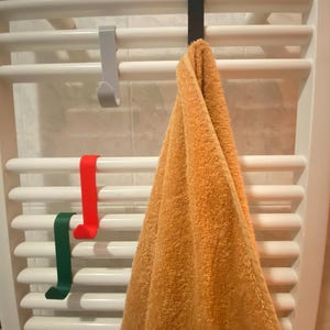Può includere: Un portasciugamani bianco con quattro ganci. Un asciugamano è appeso a uno dei ganci. L'asciugamano è arancione. Ci sono altri tre ganci sul portasciugamani. Uno è rosso, uno è verde e uno è grigio.