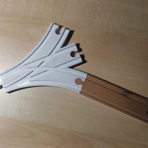 Op de afbeelding: Een wit en bruin houten treinbaanspoorstuk met een gebogen vorm en een wissel die de trein in twee richtingen kan laten rijden.