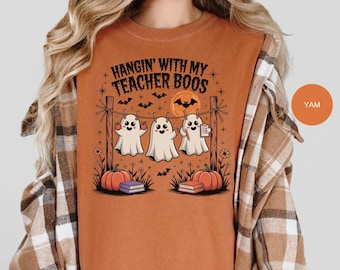 May include: Orange t-shirt with the text "Hangin' With My Teacher Boos" and a Halloween graphic. The graphic features three cartoon ghosts hanging on a clothesline with pumpkins, books, and bats.