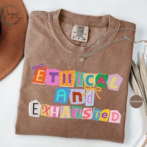 May include: A white ceramic mug with a black handle and the text "But First, Coffee" in a bold, black font. The mug is set against a blurred background, suggesting a cozy setting.