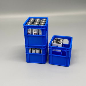 Könnte beinhalten: Zwei blaue Plastikkisten, die übereinander gestapelt sind und mit AA-Batterien gefüllt sind. Die obere Kiste hat 12 Batterien, die untere Kiste hat 6 Batterien. Die kleinere Kiste befindet sich auf der rechten Seite des Bildes.