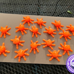 May include: A collection of orange, spider-like objects arranged on a gray surface. Each object has a central body with multiple leg-like extensions. The objects are uniformly colored and appear to be made of a solid material.