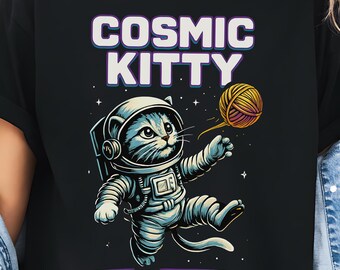 May include: Black t-shirt with the text "COSMIC KITTY" in white and purple. The graphic shows a cartoon cat in an astronaut suit playing with a ball of yarn. The word "BLACK" is in a black circle at the bottom left.