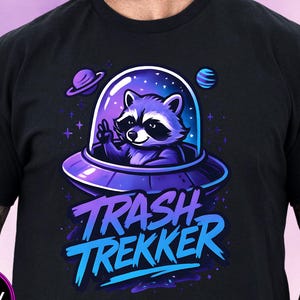 May include: Black t-shirt with a cartoon raccoon in a purple UFO, giving a peace sign. The text "TRASH TREKKER" is in blue and purple. A black circle with the word "BLACK" is in the lower left corner.