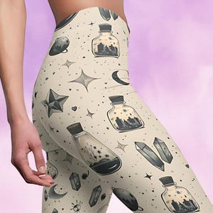 Puede incluir: Leggins beige con un patrón repetido de botellas negras, estrellas, lunas y cristales. Las botellas contienen un líquido negro con una ciudad en su interior.