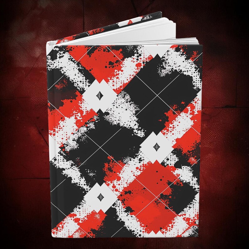 K&ouml;nnte beinhalten: Hardcover-Journal mit einem auff&auml;lligen Argyle-Muster in Schwarz, Rot und Wei&szlig;. Das Design zeigt ein Diamantgitter mit Farbspritzern und kleinen Diamantformen. Das Journal ist ge&ouml;ffnet und zeigt wei&szlig;e Seiten.
