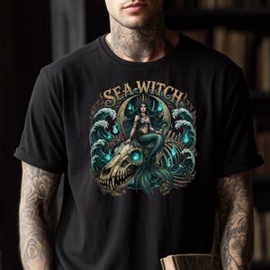 May include: Black t-shirt featuring a detailed graphic of a mermaid seated on a skull, surrounded by ocean waves and the text "SEA WITCH". The mermaid has long dark hair and a crown. The design incorporates teal and turquoise colors.