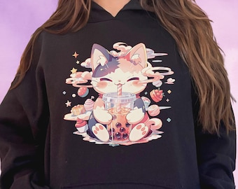May include: Black hoodie featuring a colorful illustration of a cat drinking bubble tea. The cat is depicted with pink, white, and blue fur, surrounded by sweets and clouds. The design is whimsical and playful, perfect for cat lovers.