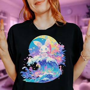 May include: A black t-shirt with a colorful graphic print of a white rabbit riding a wave with pink and blue flowers. The rabbit has pink ears and blue eyes.