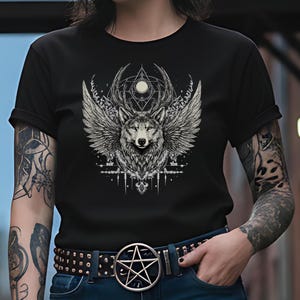 May include: Black t-shirt featuring a detailed graphic of a wolf with feathered wings, antlers, and geometric shapes. The design is in shades of gray and white. The shirt is worn with a belt with a pentagram buckle.