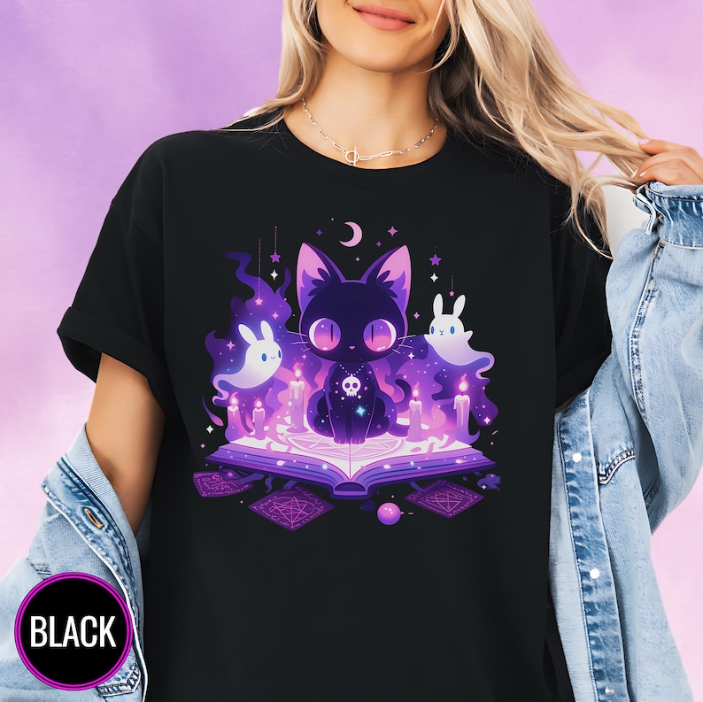 A woman wearing a black T-shirt featuring a mystical, purple-toned design of a cute black cat sitting on an open magical book, surrounded by glowing candles, floating ghost-like bunny spirits, and magical symbols. The design radiates a whimsical, witchy aesthetic against a dreamy purple background.