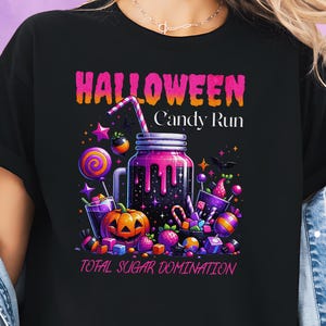 Puede incluir: Camiseta negra con un gráfico vibrante de Halloween. El diseño presenta un tarro morado con una pajita, rodeado de caramelos, una calabaza y el texto "HALLOWEEN Candy Run TOTAL SUGAR DOMINATION."