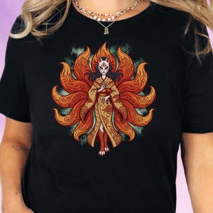 Pode incluir: Camiseta preta com uma ilustração detalhada de uma figura com máscara de raposa e quimono, rodeada por chamas laranja e vermelhas. O design tem um estilo anime japonês com detalhes intrincados e um tema místico.
