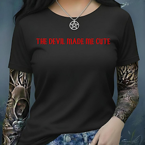 May include: Black short-sleeved t-shirt with the red text "THE DEVIL MADE ME CUTE". The shirt is worn with a silver pentagram necklace. The person has tattoos on their arms.