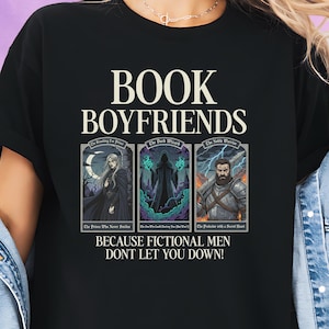 Puede incluir: Camiseta negra con la frase "BOOK BOYFRIENDS" en blanco. El diseño incluye ilustraciones de personajes de ficción y la frase "BECAUSE FICTIONAL MEN DONT LET YOU DOWN!" impresa debajo.