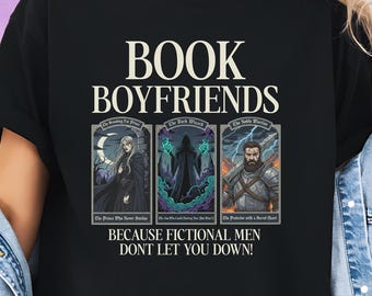 May include: Black t-shirt with the text "BOOK BOYFRIENDS" in white. Below the text are three illustrations of fictional characters. The text "BECAUSE FICTIONAL MEN DONT LET YOU DOWN!" is printed below the illustrations.