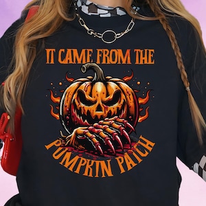 Pode incluir: Camiseta preta de manga comprida com um design de Halloween. O design apresenta uma abóbora laranja com uma expressão ameaçadora e mãos com garras, com o texto "IT CAME FROM THE PUMPKIN PATCH" em laranja.