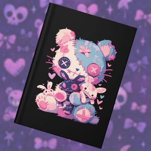 May include: Black notebook featuring a colorful illustration of a stitched teddy bear and three bunnies. The bear is white and blue with cross-stitch details and pink accents. The bunnies are pink and blue with cross-stitch details.