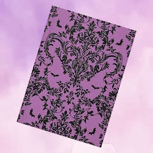 May include: A lavender notebook with a black damask pattern and bat silhouettes. The cover features a detailed floral design with swirling leaves and stems, creating a gothic or Halloween theme. The notebook is rectangular and slightly angled.