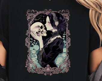 Könnte beinhalten: Schwarzes T-Shirt mit einer gotischen Illustration. Das Design zeigt eine Frau in einem schwarzen Kleid, die einen Schädel hält, umrahmt von einem verzierten Rahmen mit floralen Akzenten. Das Kunstwerk hat eine Vintage-Ästhetik mit sanften Farben.
