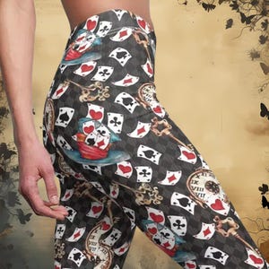 Op de afbeelding: Zwarte leggings met een herhalend patroon van speelkaarten, sleutels en een zakhorloge. De kaarten zijn rood, zwart en wit. Het zakhorloge heeft Romeinse cijfers.