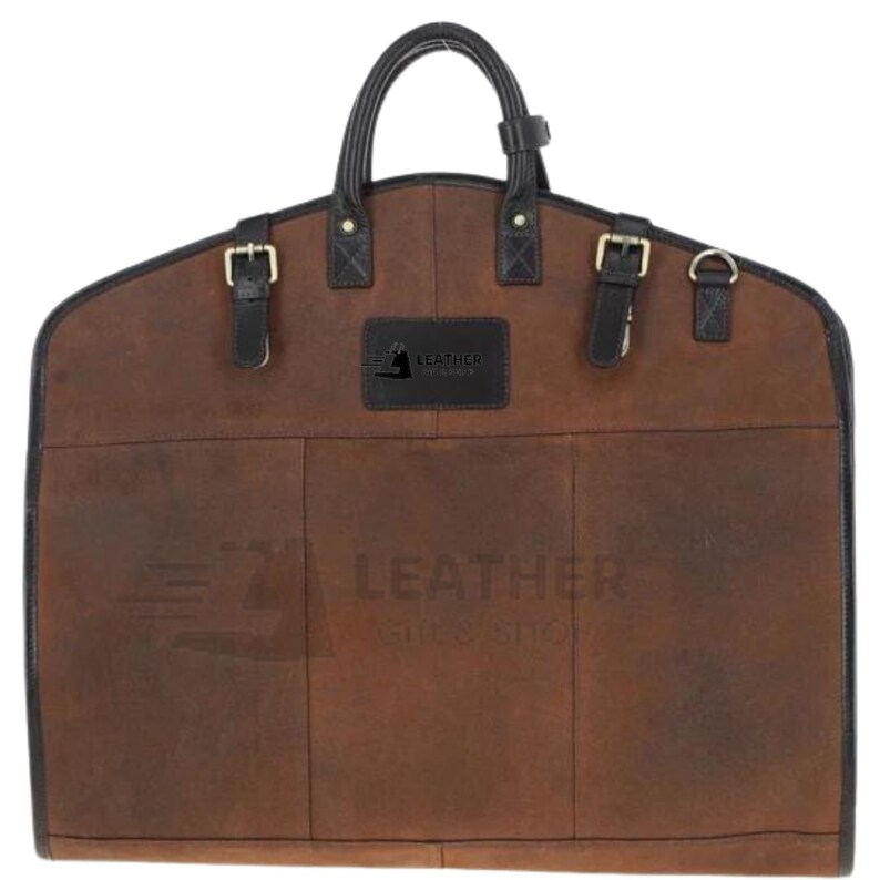 May include: Brown leather garment bag with black straps and buckles. The bag has a handle and a label that says "Leather by Artisans".