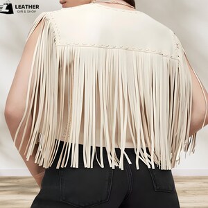 May include: A cream-colored faux leather vest with fringe detailing. The vest has a sleeveless design and a round neckline.