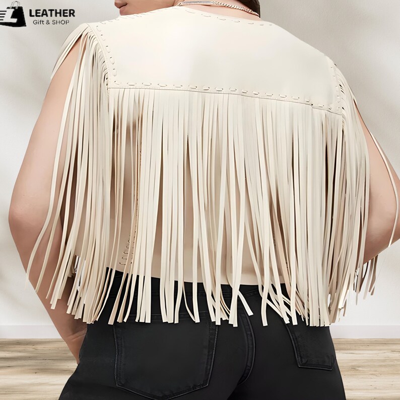 May include: A cream-colored faux leather vest with fringe detailing. The vest has a sleeveless design and a round neckline.