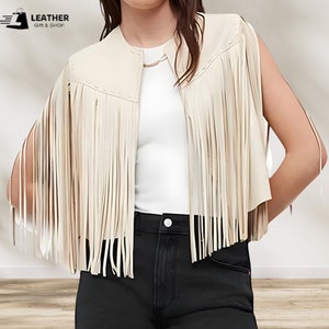 May include: A cream-colored faux leather vest with fringe detailing. The vest has a collar and a sleeveless design.  "LEATHER GIFT & SHOP" is printed in the top left corner of the image.