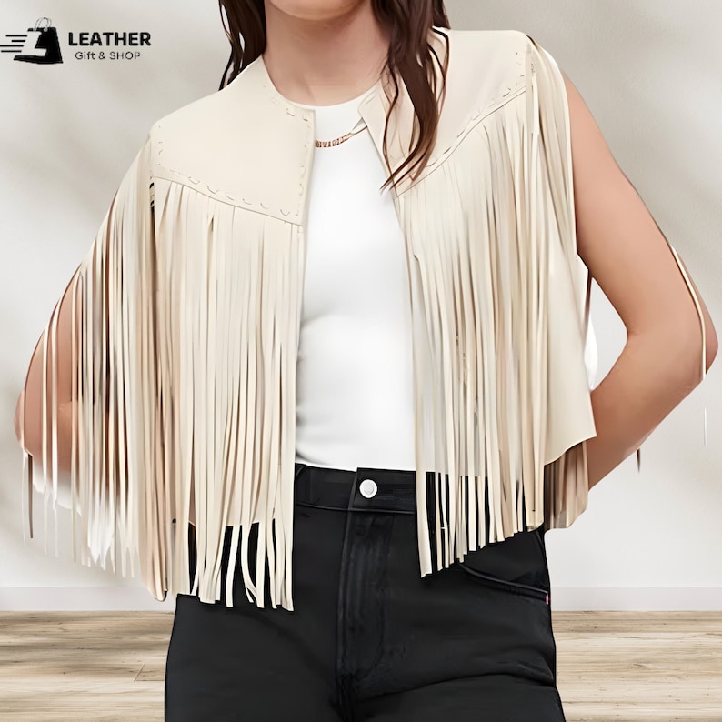 May include: A cream-colored faux leather vest with fringe detailing. The vest has a collar and a sleeveless design.  "LEATHER GIFT & SHOP" is printed in the top left corner of the image.