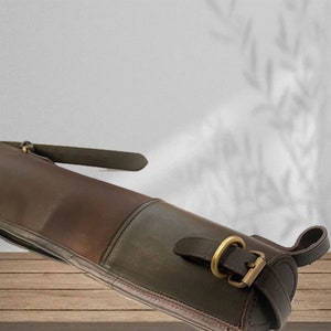 May include: A brown leather gun case with a brass buckle. The case is rolled up and has a strap.
