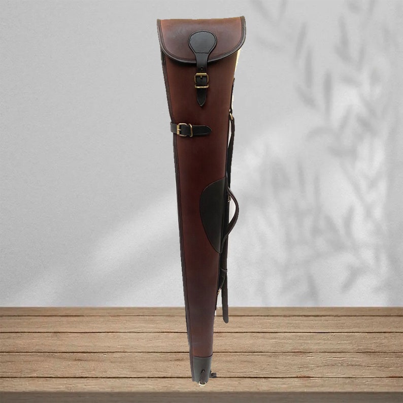 May include: A brown leather gun case with a black leather flap and a brass buckle. The case has a shoulder strap and a carrying handle.