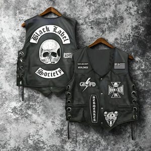 May include: Two black leather vests with patches, including "Black Label Society" and skull designs. The vests have lace-up sides and are displayed on wooden hangers. The patches feature text and graphic elements.
