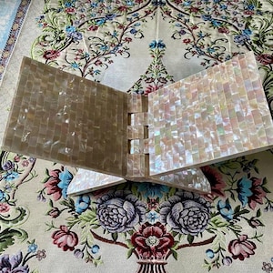 Puede incluir: Un atril decorativo hecho de azulejos iridiscentes tipo mosaico. Los paneles están en ángulo y conectados por juntas entrelazadas. La superficie brilla, reflejando la luz. Se encuentra sobre una tela con estampado floral. Un objeto decorativo.