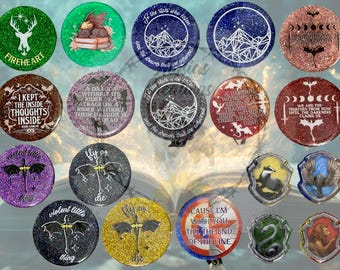 May include: A collection of circular and shield-shaped pin-back buttons featuring various fantasy-themed designs, including glittery backgrounds, dragon illustrations, celestial patterns, and text quotes such as 'Fireheart' and 'Fly or die'.