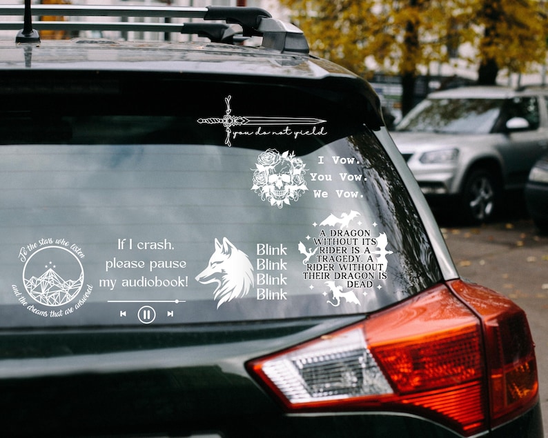 May include: A collection of white vinyl decals applied to a car rear window. Designs include a sword with the text you do not yield, a skull with roses and the text I Vow. You Vow. We Vow., a mountain graphic, a wolf, and dragon silhouettes.