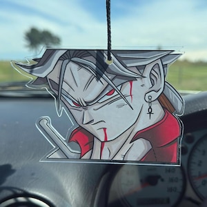 Puede incluir: Un ambientador de coche transparente de estilo anime, con un personaje de pelo gris, ojos rojos y un atuendo rojo y negro. El ambientador cuelga de una cuerda negra, con un salpicadero de coche en el fondo.