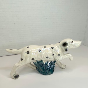 May include: White ceramic figurine of a dalmatian dog with black spots, running through green grass.