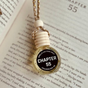 Pode incluir: Um aromatizador de carro preto e branco com o texto "Smells Like Pure Smut" e "Chapter 55". O aromatizador está pendurado em um cordão dourado e branco.
