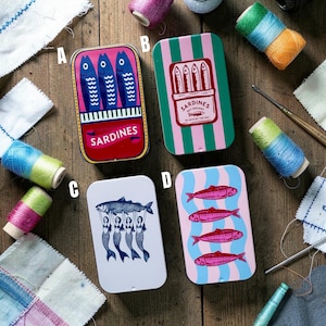 May include: Four rectangular metal tins labeled A, B, C, and D. Tin A features blue fish on a red background. Tin B has green and pink stripes with a sardine graphic. Tin C shows mermaids holding a fish. Tin D displays pink fish on blue waves.