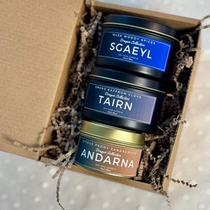 Puede incluir: Tres velas de cera de soja en una caja de regalo. Las velas est&aacute;n etiquetadas como "Sgaeyl", "Tairn" y "Andarna". Cada vela tiene un aroma y un color diferentes.