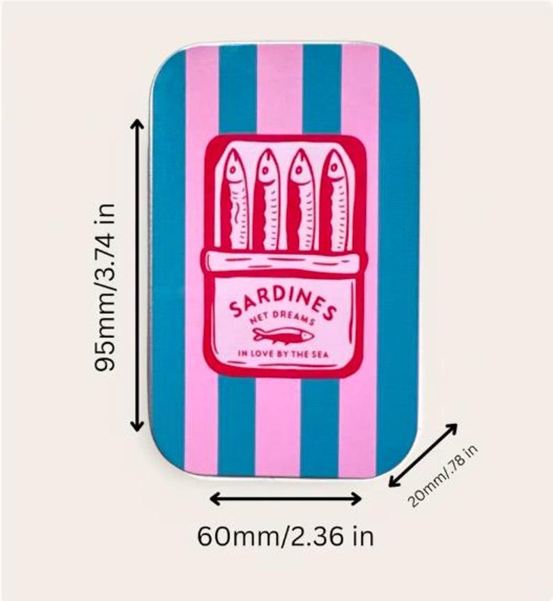 May include: A rectangular metal tin featuring vertical pink and teal stripes. The center displays a graphic of four sardines in a box with the text SARDINES NET DREAMS IN LOVE BY THE SEA. Dimensions are 3.74 inches by 2.36 inches by 0.78 inches.