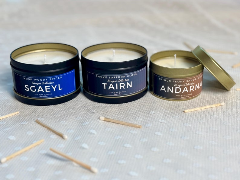 Puede incluir: Tres peque&ntilde;as latas redondas de velas negras con tapas doradas. Las velas est&aacute;n etiquetadas con los nombres "Sgaeyl", "Tairn" y "Andarna" y los aromas "Musk Woody Spices", "Smoke Saffron Clove" y "Citrus Peony Sandalwood".