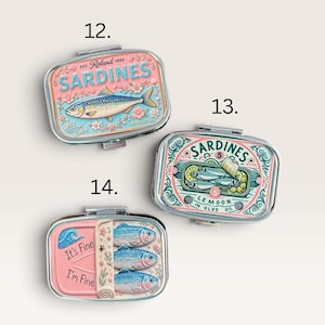 May include: Three rectangular metal tins with hinged lids, labeled 12, 13, and 14. Tin 12 features a pink sardine illustration. Tin 13 shows sardines with lemon slices and ornate green scrollwork. Tin 14 is pink with three fish and the text It's Fine I'm Fine.