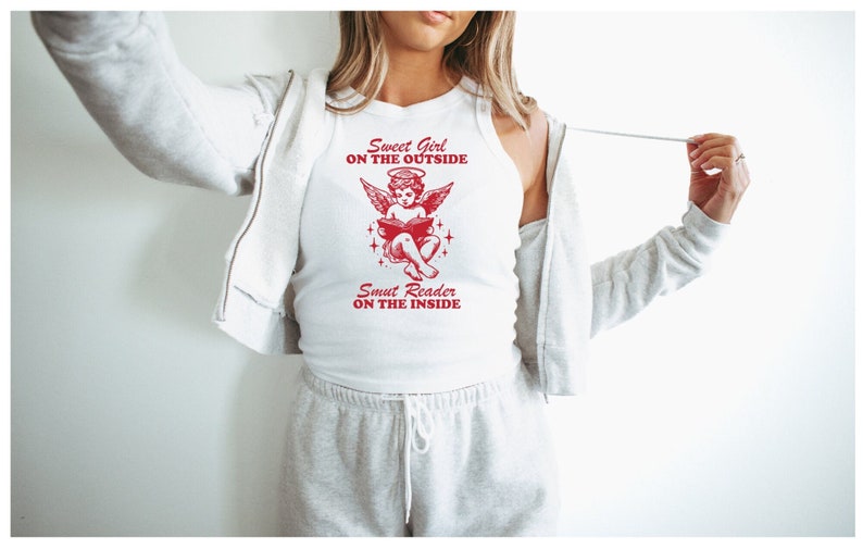 Puede incluir: Camiseta blanca de tirantes con un gr&aacute;fico rojo de un &aacute;ngel leyendo un libro. El gr&aacute;fico dice "Sweet Girl on the Outside" y "Smut Reader on the Inside".